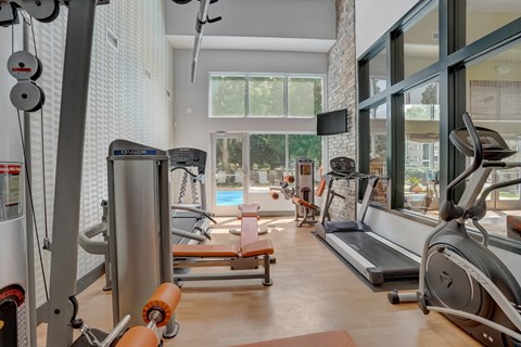 Gym with exercise equipment and a large window with a pool in the background at Governor's Park, Fort Collins, 80525